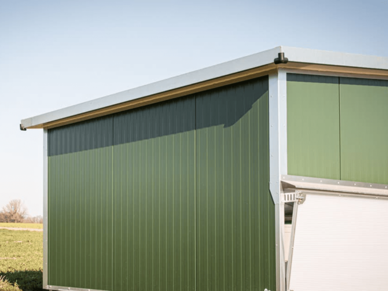 Der Alt-Text beschreibt einen mobilen Hühnerstall mit grüner Wandverkleidung und metallischem Dach.