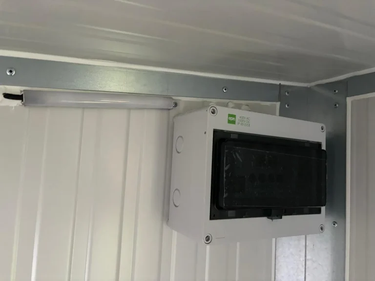 Ein Lichtsteuerungskasten und eine Leuchte sind an einer Wand aus Metallpaneelen montiert.