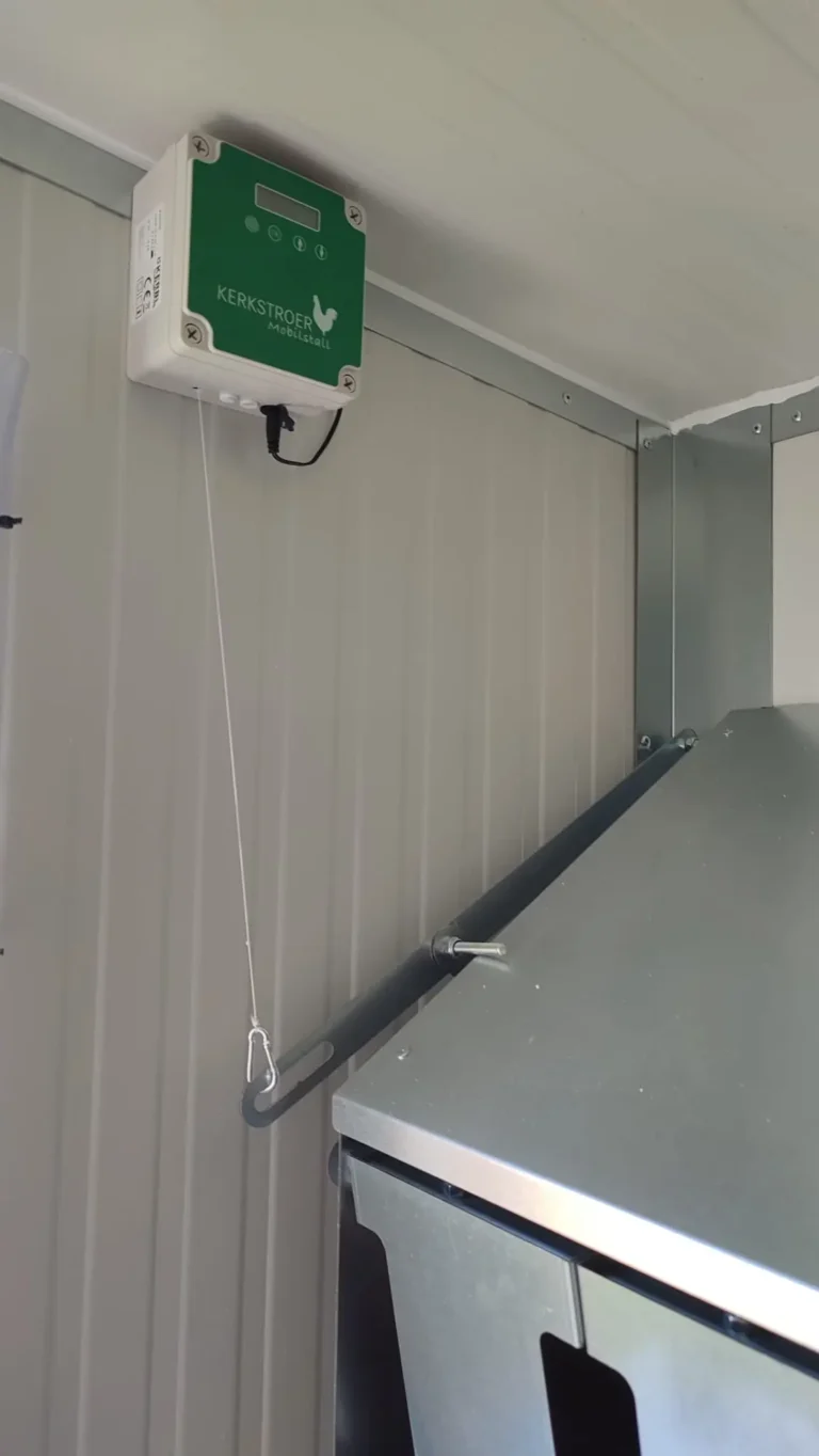 Ein automatisches Neststeuergerät mit digitaler Anzeige ist an der Wand eines Hühnerstalls montiert.